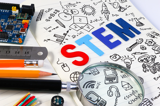 Portrait of ruler, pencil, magnifying glass and circuit board with paper that says STEM