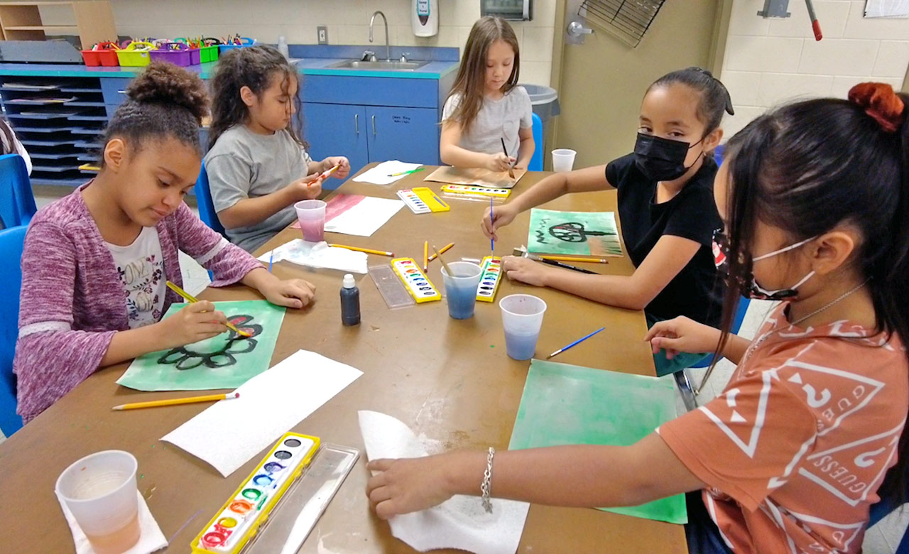 Group of students at a table in the classroom painting.