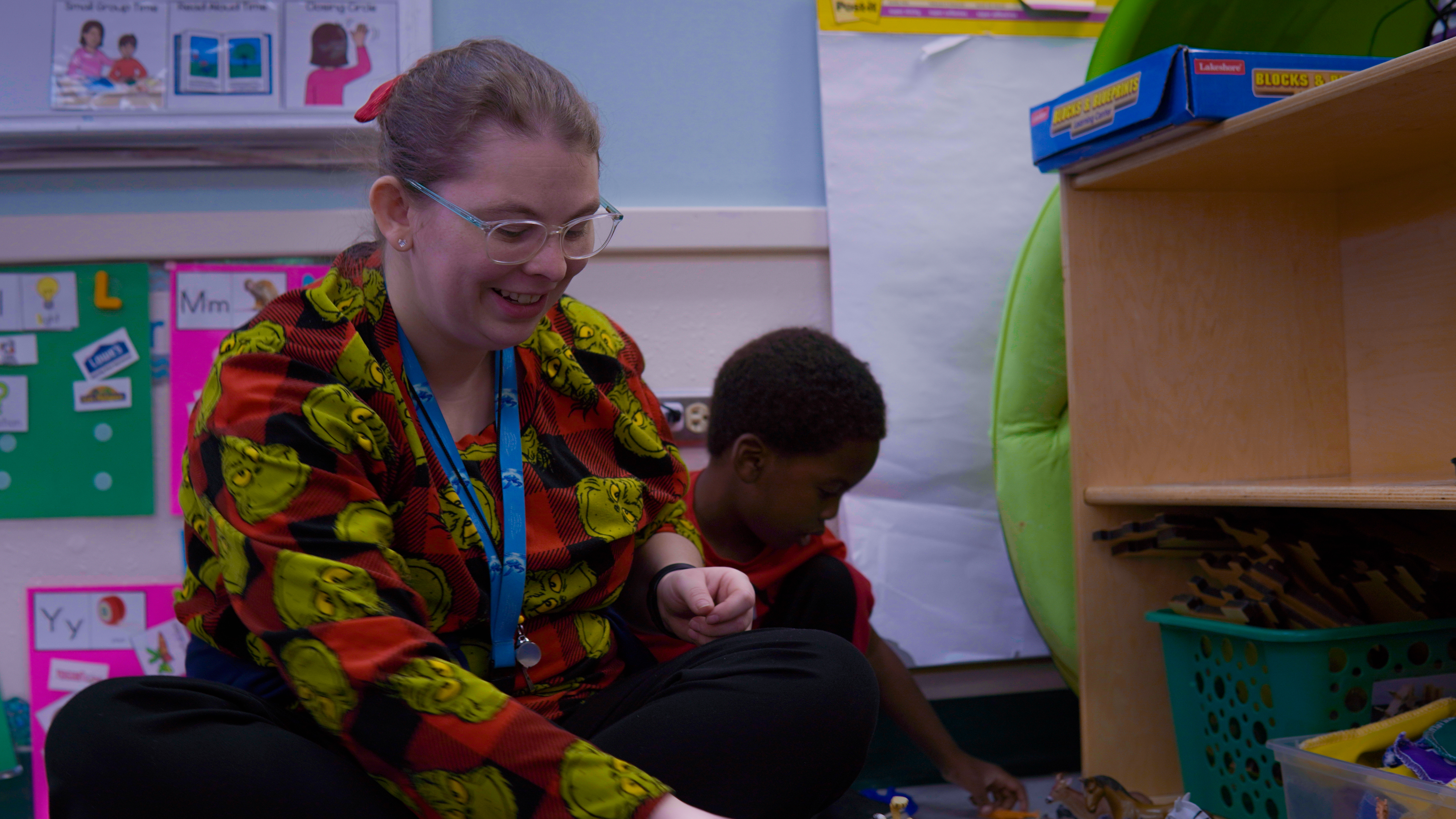 Instructional Assistant, Ms Haskins, sitting on the floor with one of her Pre-K students