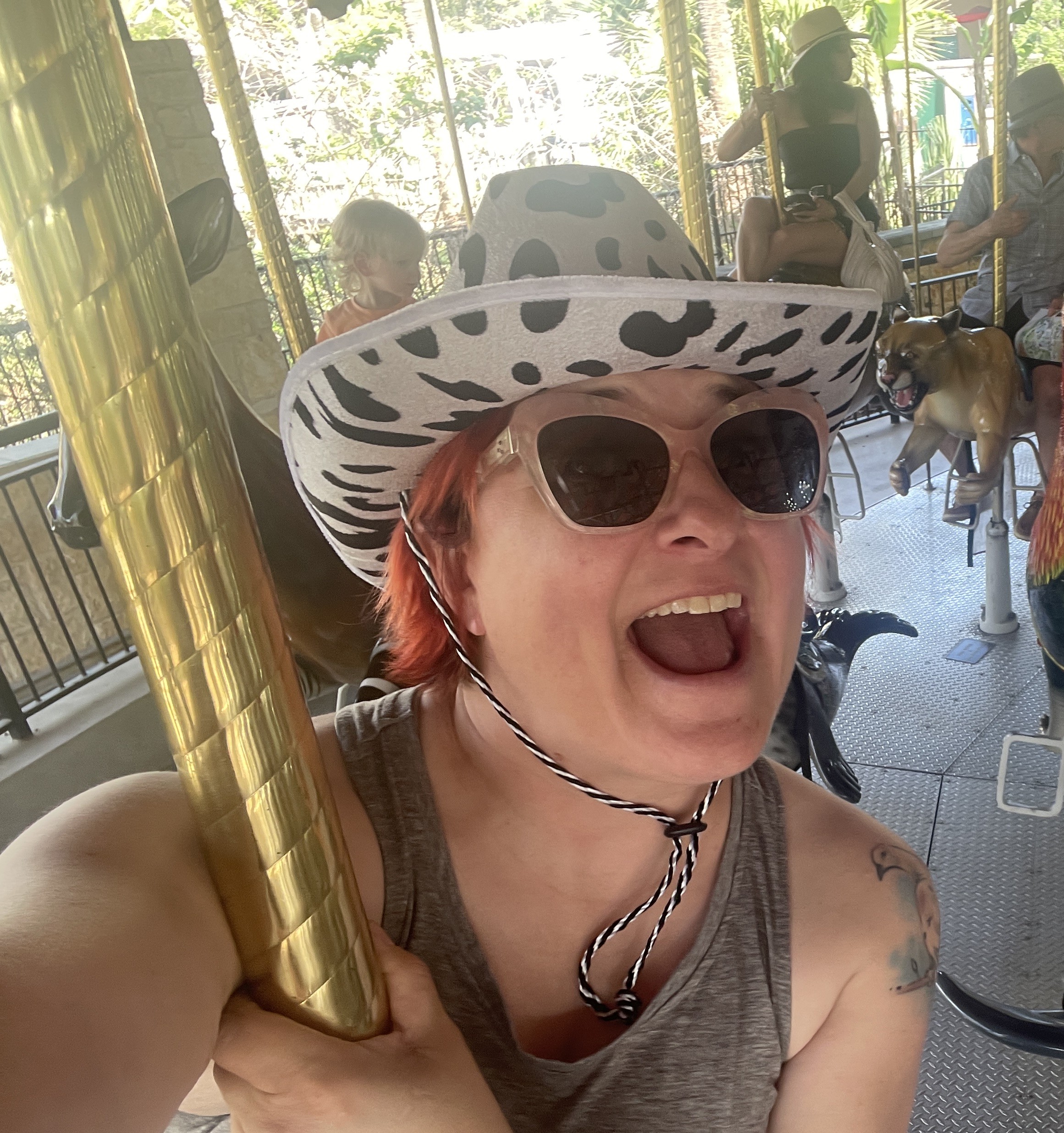 Librarian wearing a cow-print cowboy hat while riding a carousel.
