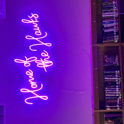 Purple neon sign above book cases that reads "Home of the Hawks"