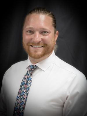 White man wearing a white dress shirt and black tie with blue, white and pink flowers.