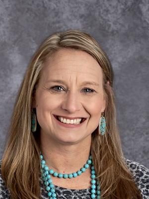 Ms. Nelson wearing a blue beaded necklace with matching earings. Blonde hair, bright smile.